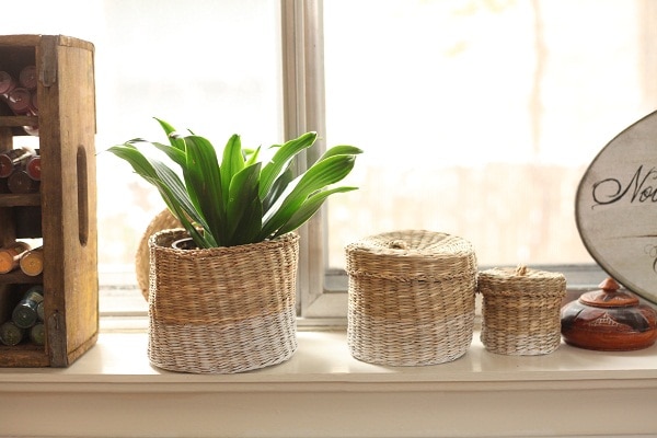 3 wicker baskets on a window ledge with a plant inside of one. 