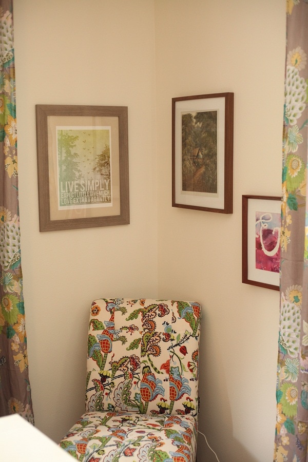 Reading corner in a studio room, with a brightly printed upholstered chair and framed art on the wall. 