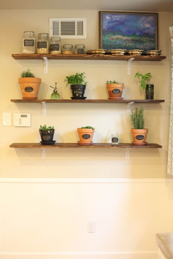 Finished indoor herb garden, featuring three wooden shelves lined with various pots and planters filled with herbs. 