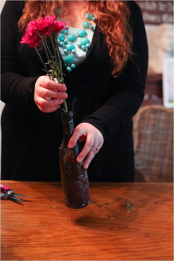 Putting pink flowers into an old glass bottle 