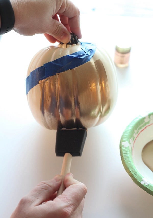 Brushing the bottom half of a pumpkin with liquid gold leaf.