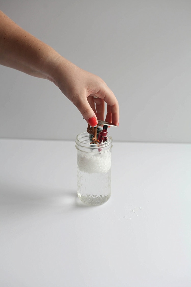 Figurines being put upside down into a snow globe mason jar filled with water and snow
