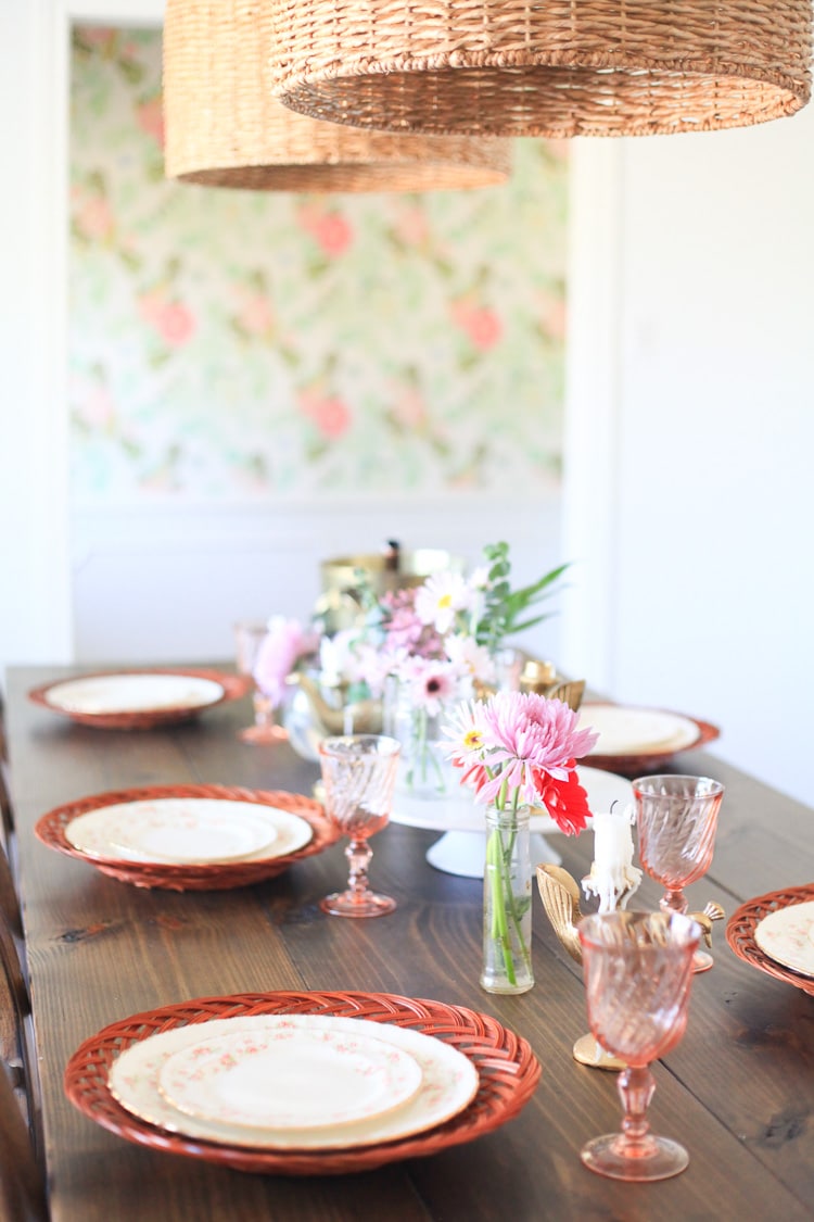 A close up of a dining room table with brightly colored chargers, floral china plates and pink glasses, perfect for Spring!