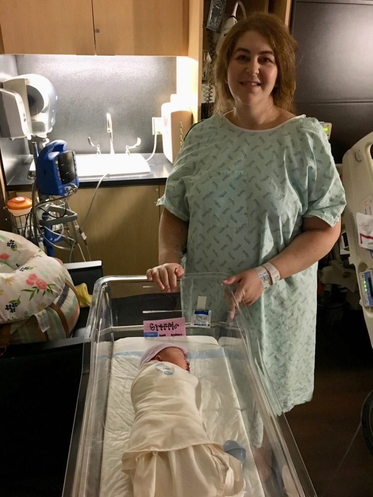 Mother standing by swaddled newborn in a bassinet in hospital room