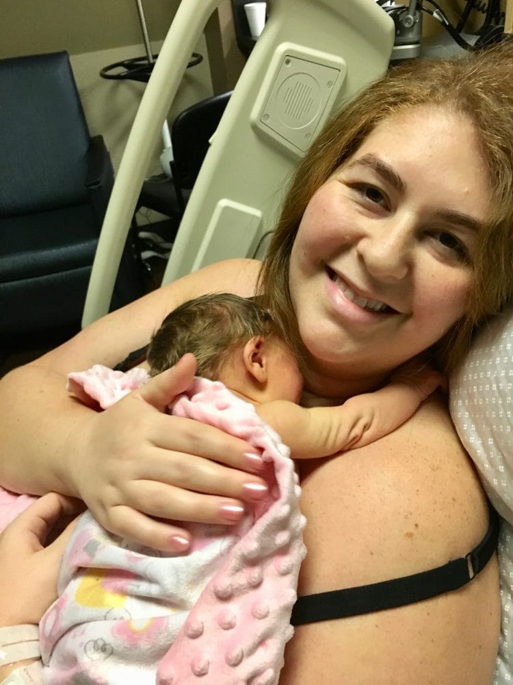 Woman smiling after delivery with newborn baby wrapped in blanket hugging her neck