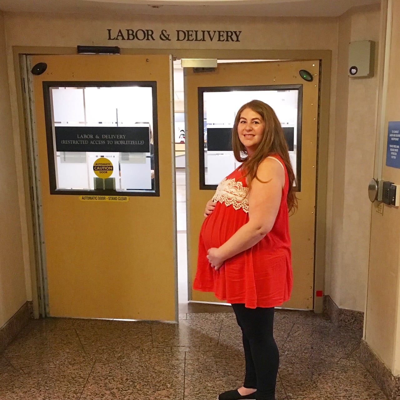 pregnant woman with red hair standing in front of labor and delivery wing in hospital about to deliver baby