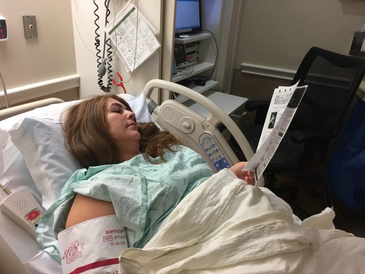 Pregnant woman lying in hospital bed reading paperwork
