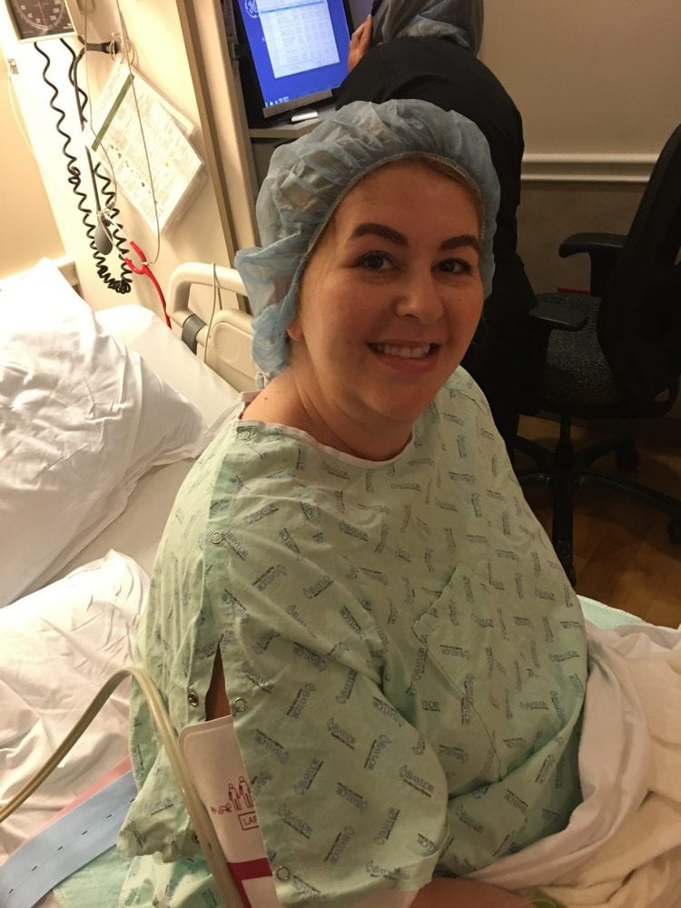 Pregnant woman in hospital scrubs smiling in hospital bed with blue sterile cap on head