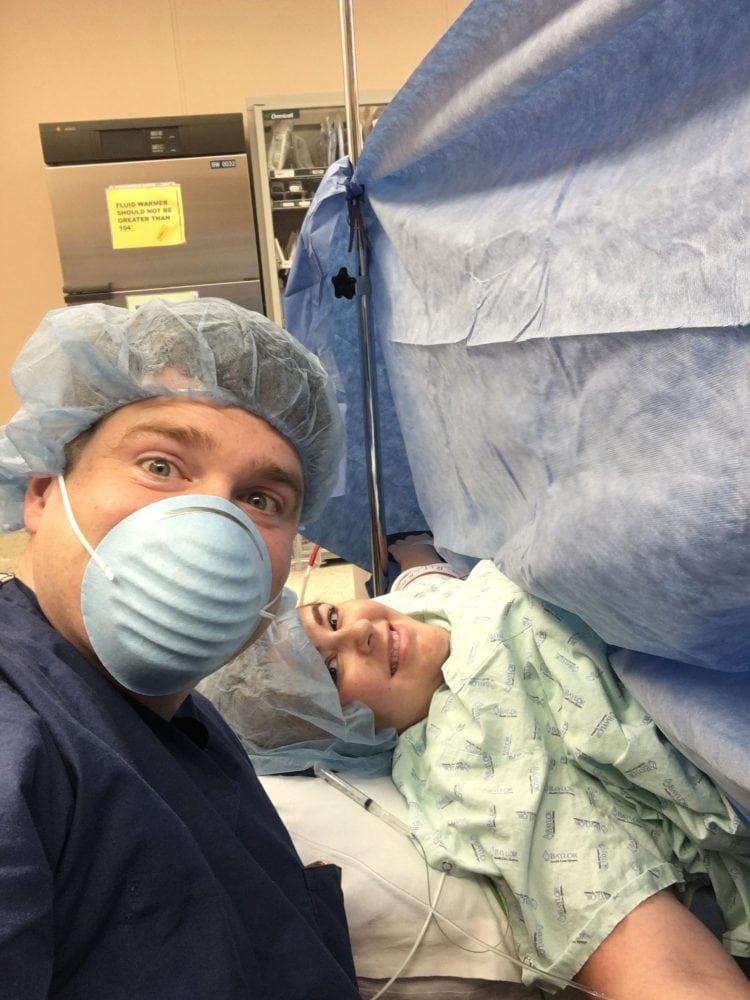 Couple smiling in delivery room during c-section with blue screen up