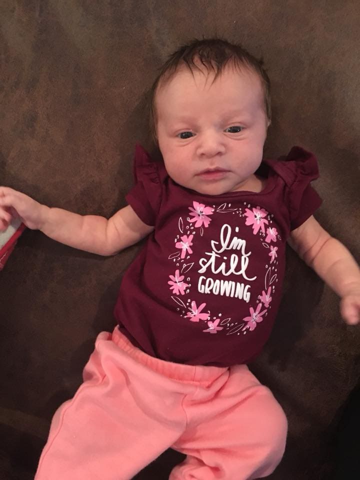 Newborn baby girl in a maroon onsie that says I'm still Growing