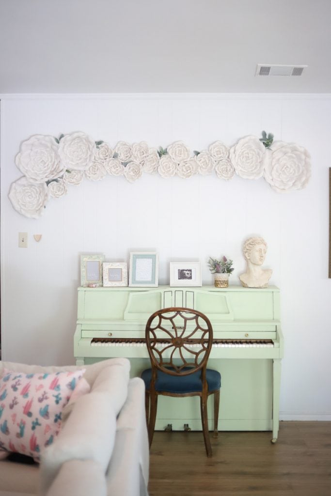 White flower wall decor hanging on a living room wall above a mint piano.