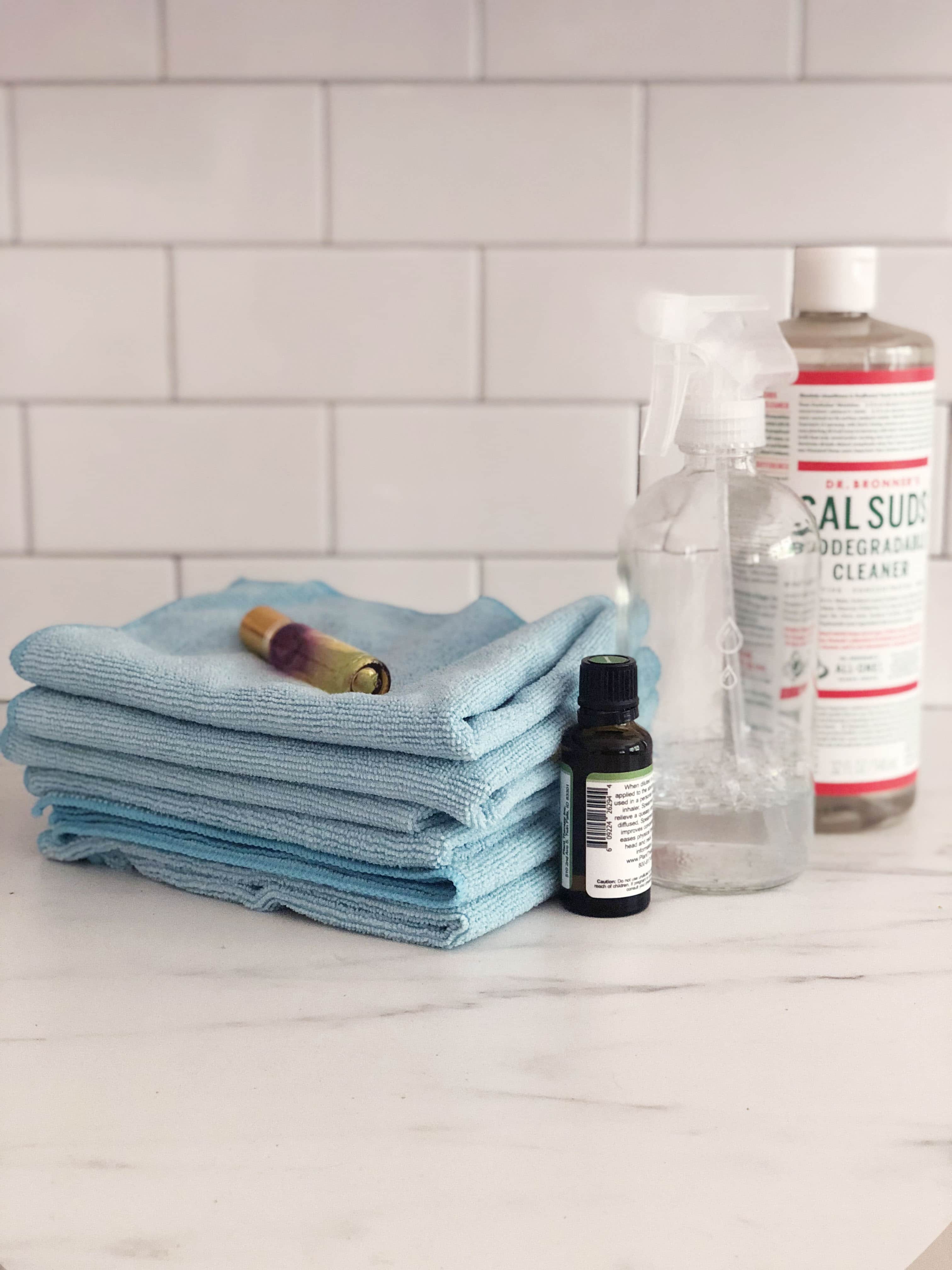 Blue microfiber rag, glass bottle, sal suds soap, and essential oils to make a natural cleaning spray. 