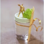 Mason jar with blue lid and clear liquid inside. The jar has a gold deer glued to the top