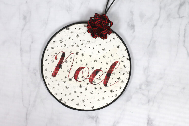 Round ornament made from an embroidery hoop with plaid noel lettered on it.