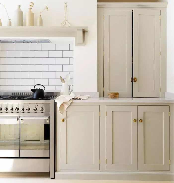 Warm, creamy beige kitchen cabinets look inviting next to a stainless steel gas stove and white subway tile. Kitchen cabinet paint color: Peau de Soie by Benjamin Moore.