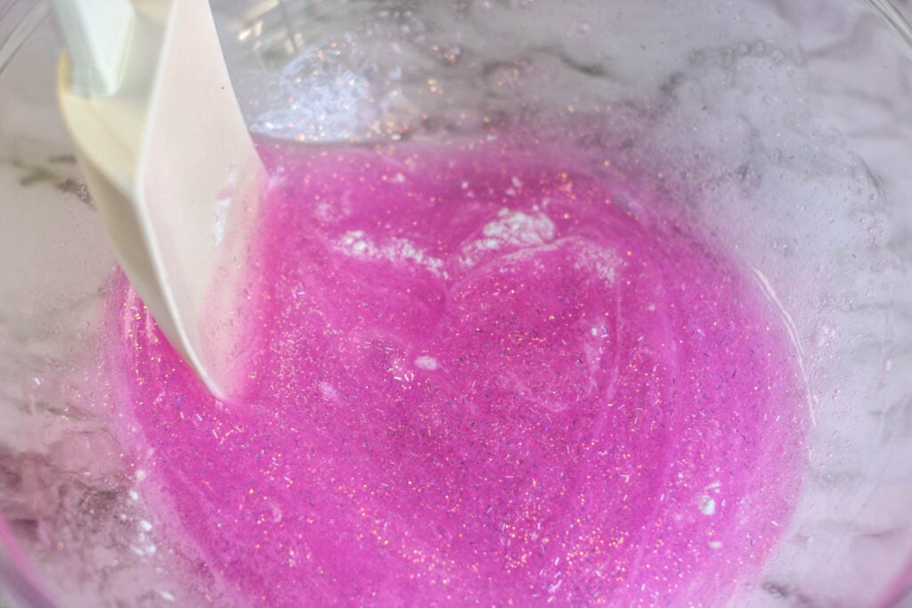 Adding baking soda to pink glitter glue and mixing to combine to make DIY unicorn slime.
