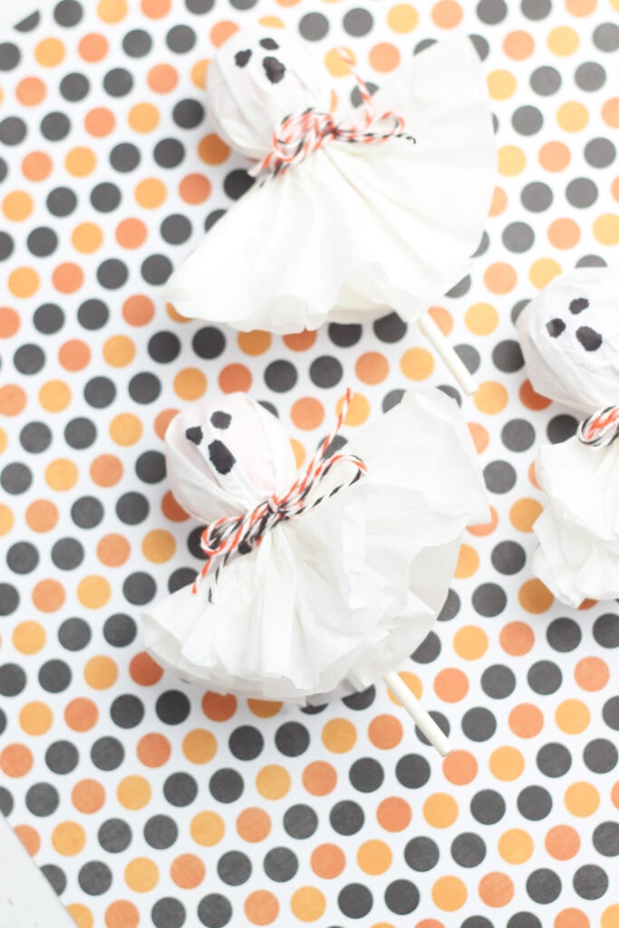 Ghost lollipops made from Tootsie Pops, coffee filters and twine against a Halloween polka dot color scheme.