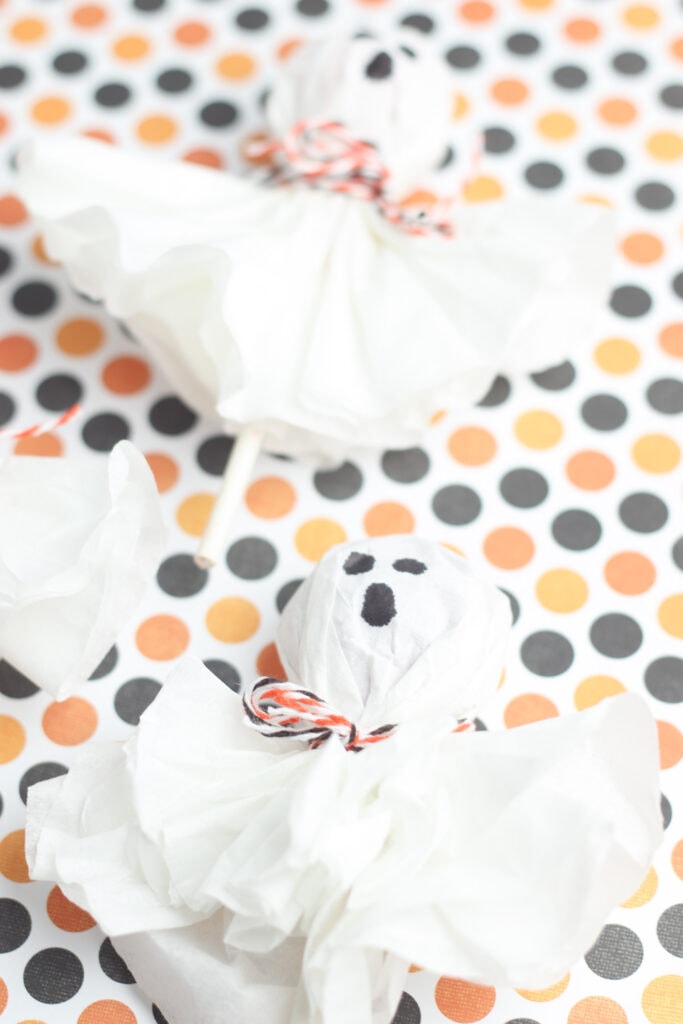 Ghost lollipops made from Tootsie Pops, coffee filters and twine against a Halloween polka dot color scheme.