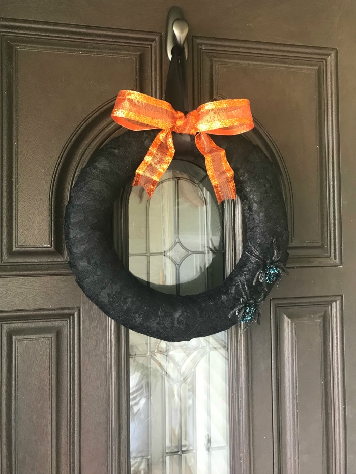 Black lace Halloween wreath with spiders and orange bow hung on a door.
