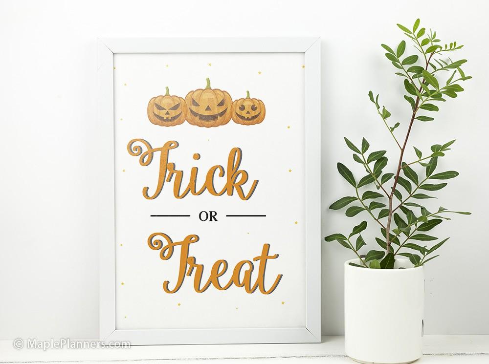 Printable Trick or Treat Halloween wall art in a white frame next to a plant.