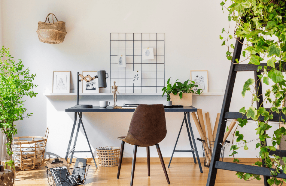 Light bright and airy office with a black desk and a brown chair with lots of plants in the room. Baskets for storage.