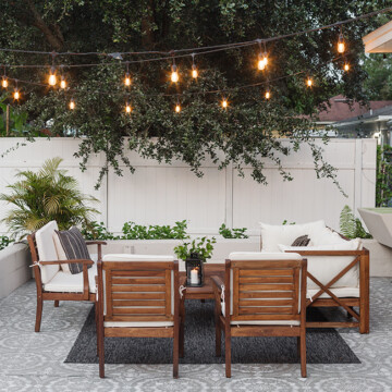 Outdoor patio furniture set outside under trees with lights in the trees. The flooring is an outdoor carpet.