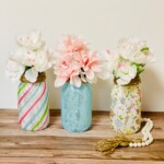 Three mason jar flower vases on a wood countertop.