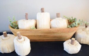 White fabric pumpkins made with sawed off rolls of toilet paper styled elegantly in a wooden bowl and greenery make great DIY Halloween decorations.