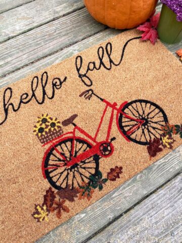Doormat that reads hello fall picturing a bicycle and some flowers