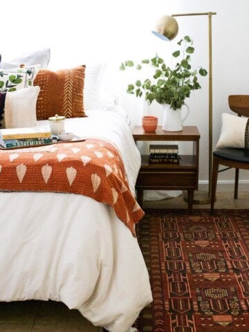 Fall Bedroom Decor - Fall inspired bedroom setting with a cozy orange blanket at the foot of the bed and orange throw pillows and an orange candle on the bedside table.