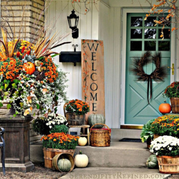 Front door and porch area decorated for the fall with pumpkins and brightly colored fall leaves and flowers with a welcome sign.