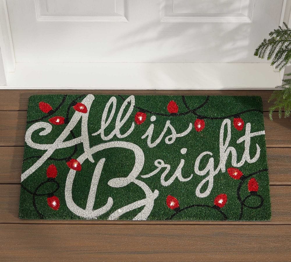 Green door mat with red Christmas lights reading All is Bright.