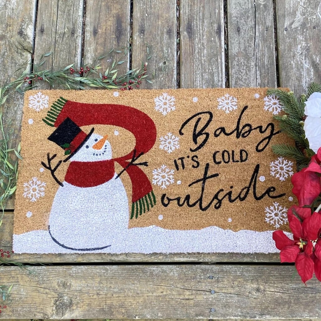 a snowman on an outdoor mat with Christmas song lyrics beside him
