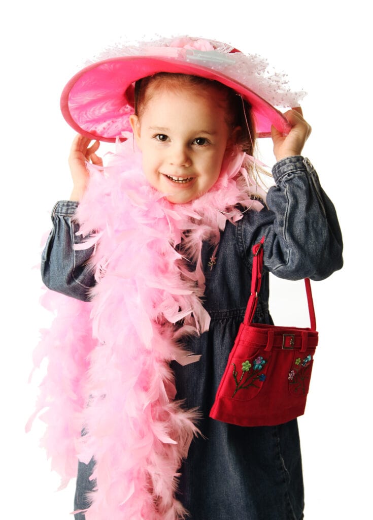 Portrait of an adorable preschool girl playing dress up with a fancy hat, purse, and pearl necklace isolated on white