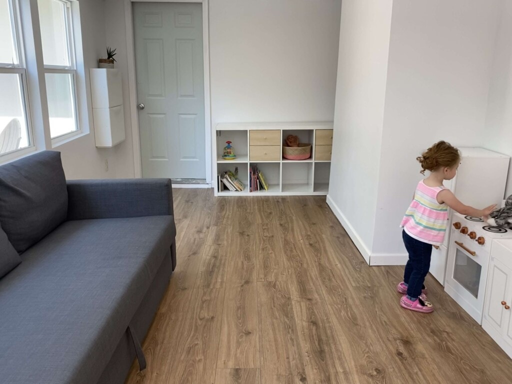 Sunroom/Playroom with a white play kitchen and little girl playing. 