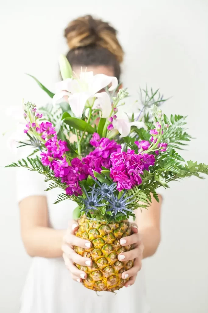 woman holding a hollowed out pineapple with flowers