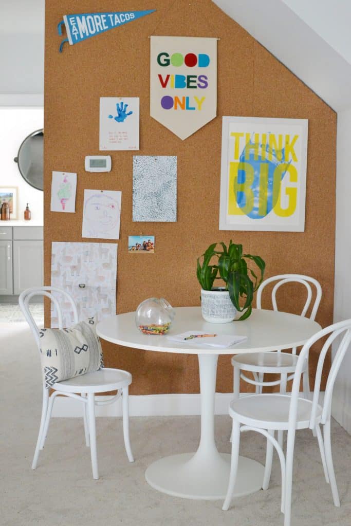 a small dining nook with a cork board wall covered in assorted art prints and pictures