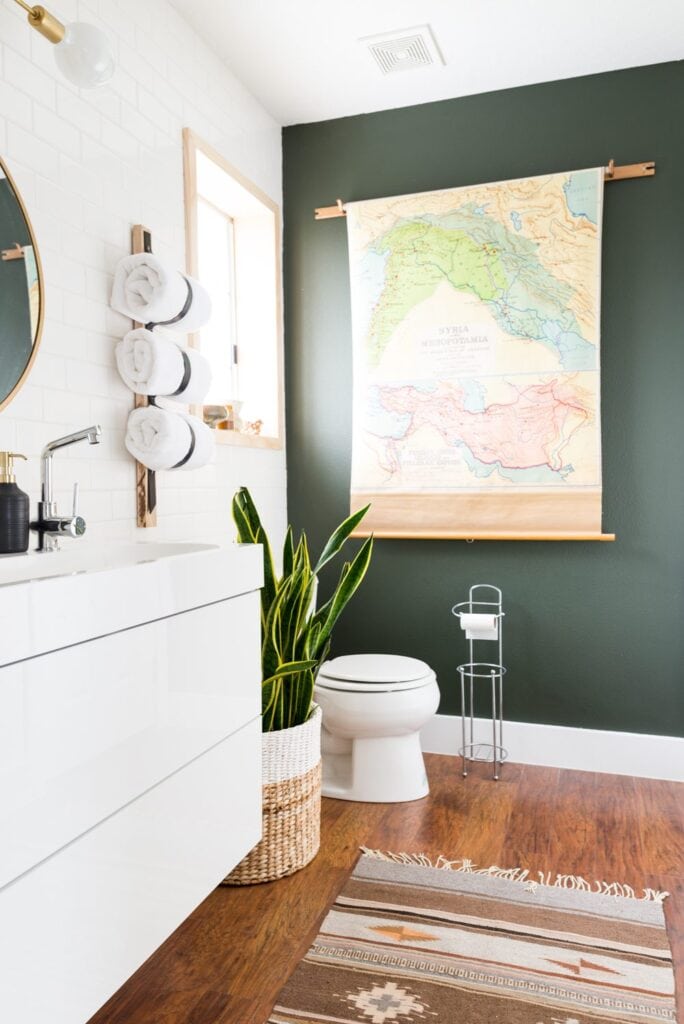 brightly lit bathroom with dark green accent wall with a map hung on it