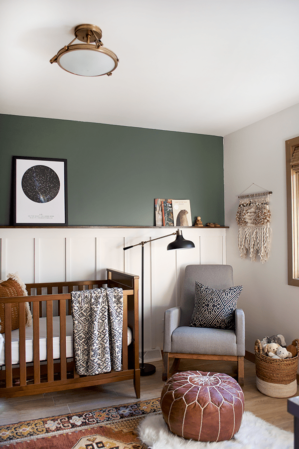 nursery with board and batten against a green accent wall and brown toned furniture