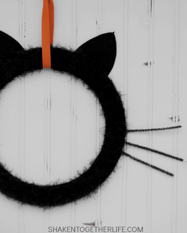 Round black felted cat wreath with ears, hung by an orange ribbon.