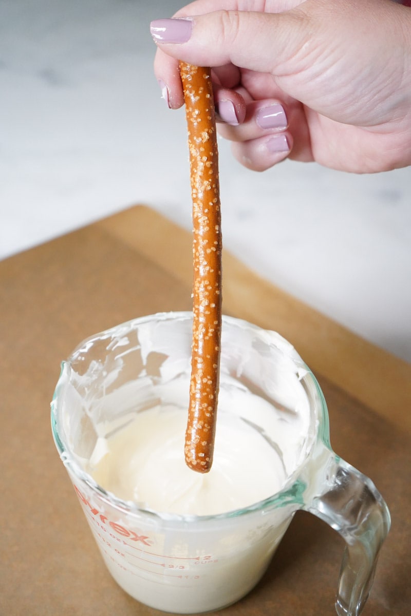 Dipping a single pretzel rod into a measuring cup of candy melts.