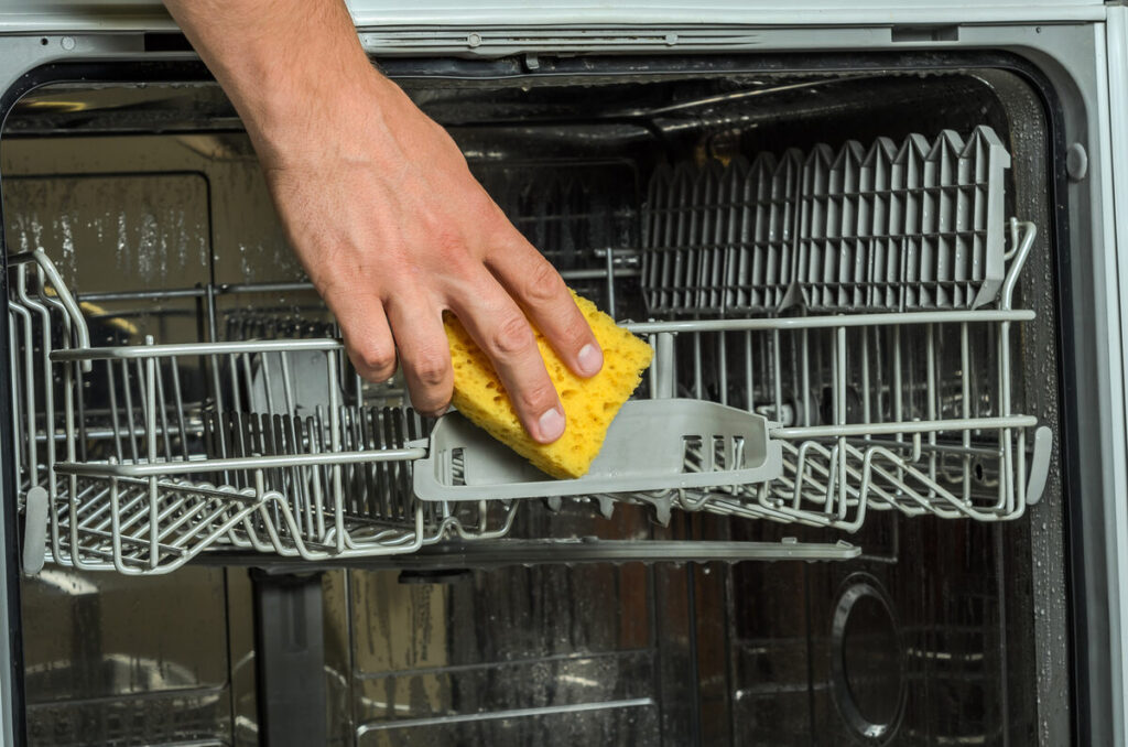man using a sponge to wipe down dishwasher interior racks