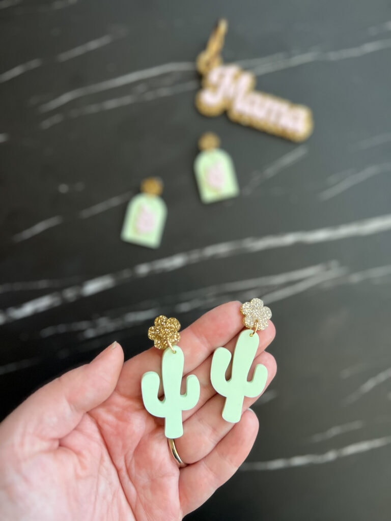 Holding a pair of gold and mint green laser cut cactus earrings.
