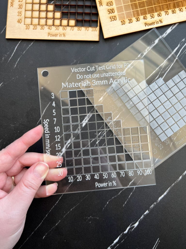 Holding up a piece of acrylic with measurements listed on it.