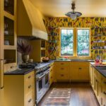 Kitchen with yellow cabinets, walls, and ceilings. The wall straight ahead has wallpaper and open shelving on either side of a window.