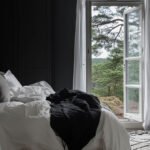 dark room with white bedding, curtains, and open door letting in the breeze