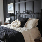 black paneled accent wall behind a wrought iron bed