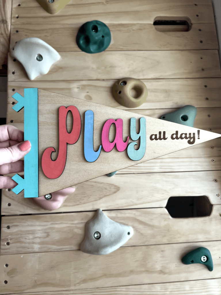 Wooden pennant in front of a climbing wall that says "play all day"