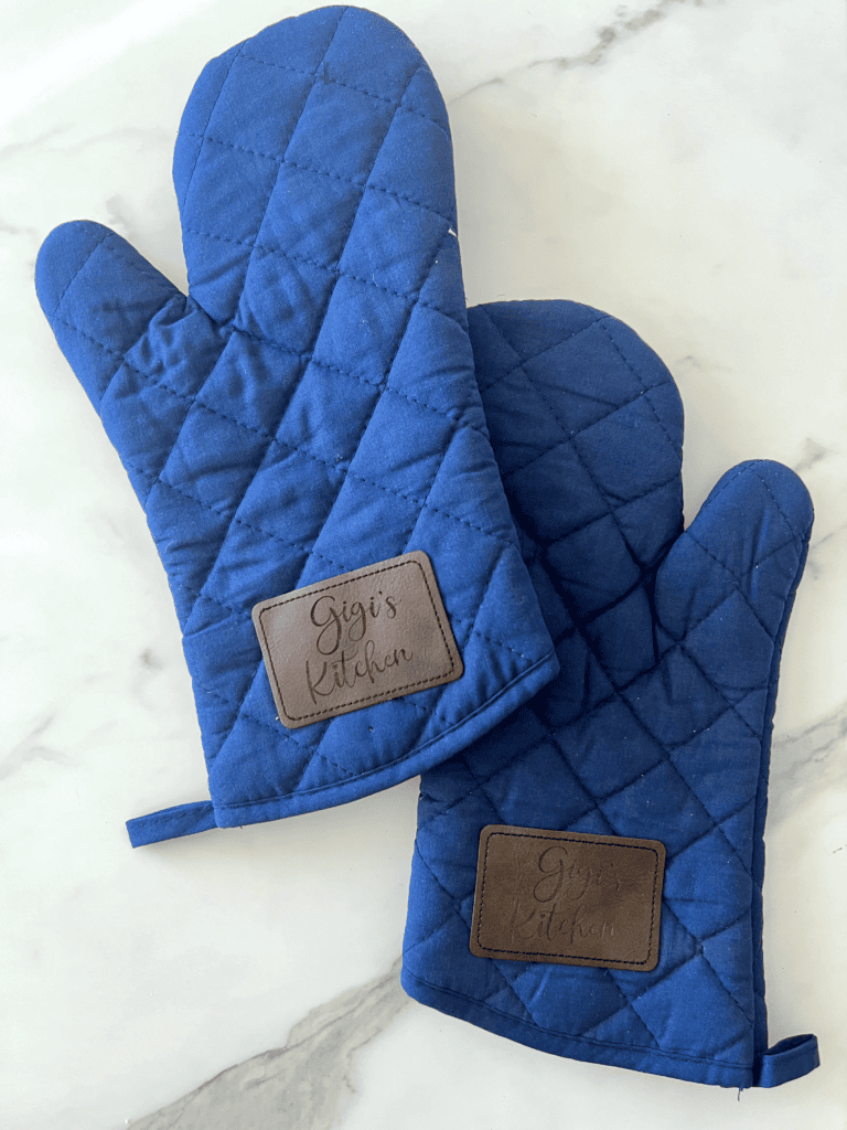 Pair of blue oven mitts that say "gigi's kitchen" on leather engraved patches