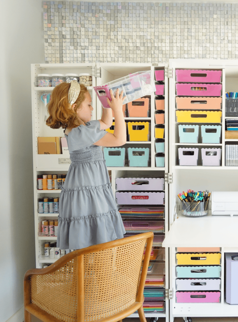 Girl standing on a chair to reach a box in a craft cabinet